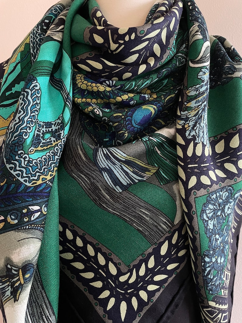 Peut inclure: Un foulard carr&eacute; &agrave; motifs dans les tons de turquoise, vert, marine et cr&egrave;me. Le foulard pr&eacute;sente des motifs complexes, notamment des plumes stylis&eacute;es et des motifs floraux. Les bords sont bord&eacute;s d'une bordure vert fonc&eacute; et marine.