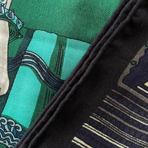 Peut inclure: Gros plan sur un foulard &agrave; motifs avec une bordure bleu marine fonc&eacute;. Le foulard pr&eacute;sente un motif avec des nuances de vert, de sarcelle et de bleu marine. Le tissu a un aspect textur&eacute;, avec un motif de tissage en diagonale visible.
