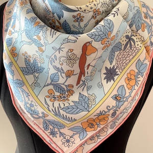 May include: Square silk scarf with a floral and bird design. The scarf features a light blue background with orange and blue flowers, green leaves, and a brown bird. The border is pink with a yellow accent.