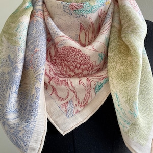 Op de afbeelding: Een witte zijden sjaal met een bloemenprint in tinten blauw, groen en rood. De sjaal is gevouwen en gedrapeerd over de nek van een mannequin.