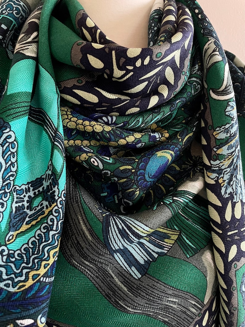 Peut inclure: &Eacute;charpe &agrave; motifs verts et bleus, avec des motifs floraux et abstraits. L'&eacute;charpe pr&eacute;sente des couleurs sarcelle, marine et vert olive. Le tissu semble doux et fluide, avec un tissage en chevrons subtil. L'&eacute;charpe est pli&eacute;e.