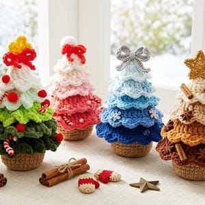 May include: A collection of handmade crochet Christmas trees in various colors, including green, white, pink, and blue. Each tree is adorned with decorative elements like bows, stars, and cinnamon sticks. The trees are displayed on a table with a snowy window background.