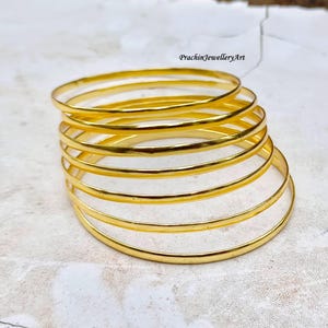 Puede incluir: Un conjunto de ocho brazaletes de oro, dispuestos en forma circular. Los brazaletes son lisos y brillantes, con un borde ligeramente redondeado.