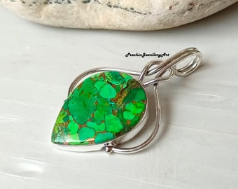 May include: A silver pendant with a green and brown turquoise stone. The stone is set in a silver bezel and the pendant has a bail for attaching a chain.
