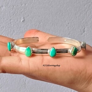 May include: A silver cuff bracelet featuring four teardrop-shaped turquoise stones set along the band. The metal has a polished finish, and the text 925Silverringshop is visible in the centre. The bracelet has an open design for adjustment.
