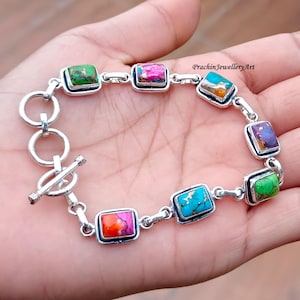 Puede incluir: Una pulsera de eslabones de plata con siete piedras rectangulares de varios colores, incluyendo verde, rosa, naranja, azul y morado. La pulsera incluye un cierre de barra y el texto PrachinJewelleryArt es visible en la esquina superior derecha.