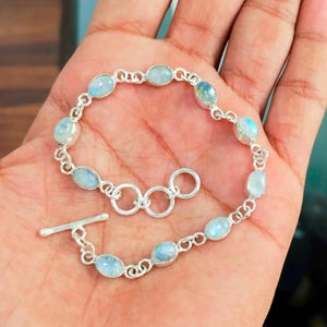 May include: A silver bracelet with oval-shaped moonstone beads. The bracelet has a toggle clasp and a chain link design.