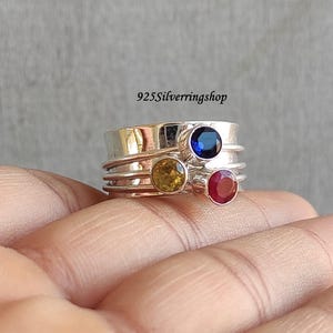 Peut inclure: Une bague tournante en argent avec trois pierres précieuses : un saphir bleu, une citrine jaune et un rubis rouge. 925Silverringshop.