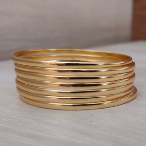 May include: A stack of six gold-colored bangle bracelets. The bracelets are all the same width and have a smooth, shiny finish.
