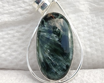 Peut inclure: Un pendentif en argent avec une pierre précieuse verte et blanche. La pierre précieuse est de forme ovale et présente un motif tourbillonnant. Le pendentif est sur un fond blanc.