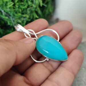 Puede incluir: Un colgante de piedra preciosa azul turquesa con un engaste en forma de corazón plateado. El colgante está en una cadena de plata.
