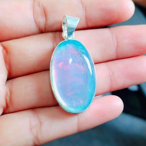 Può includere: Un ciondolo d'argento con una grande pietra ovale blu iridescente. La pietra preziosa ha una tonalità rosa chiaro e una finitura scintillante.