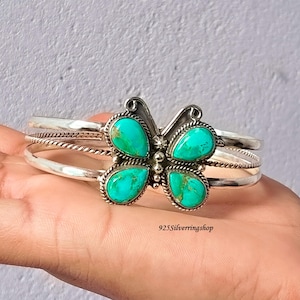 May include: A silver cuff bracelet featuring a butterfly-shaped centrepiece with four teardrop-shaped turquoise stones. The band consists of two smooth silver wires and one twisted silver wire. The text 925Silverringshop is visible on the image.