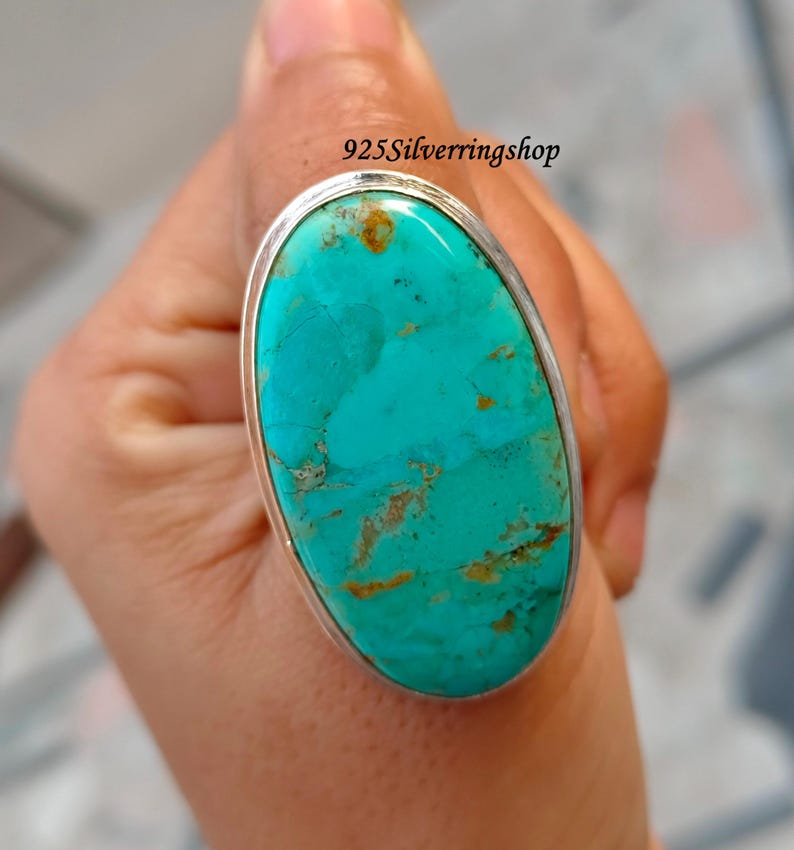 May include: A large oval turquoise ring with a silver band. The turquoise stone has brown and tan matrix patterns. The ring is set in a silver bezel.