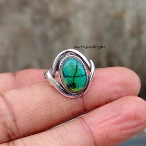 May include: A silver ring with an oval-shaped green and blue gemstone set in a twisted silver band.