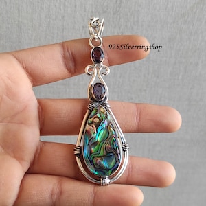May include: A silver pendant with a teardrop-shaped abalone shell and two purple amethyst stones. The pendant is on a silver chain.