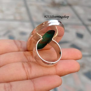 May include: A silver ring with a large, oval turquoise stone. The ring has a wide band and a polished finish. The stone is a vibrant turquoise color with brown and green marbling. The text "925Silverringshop" is visible.