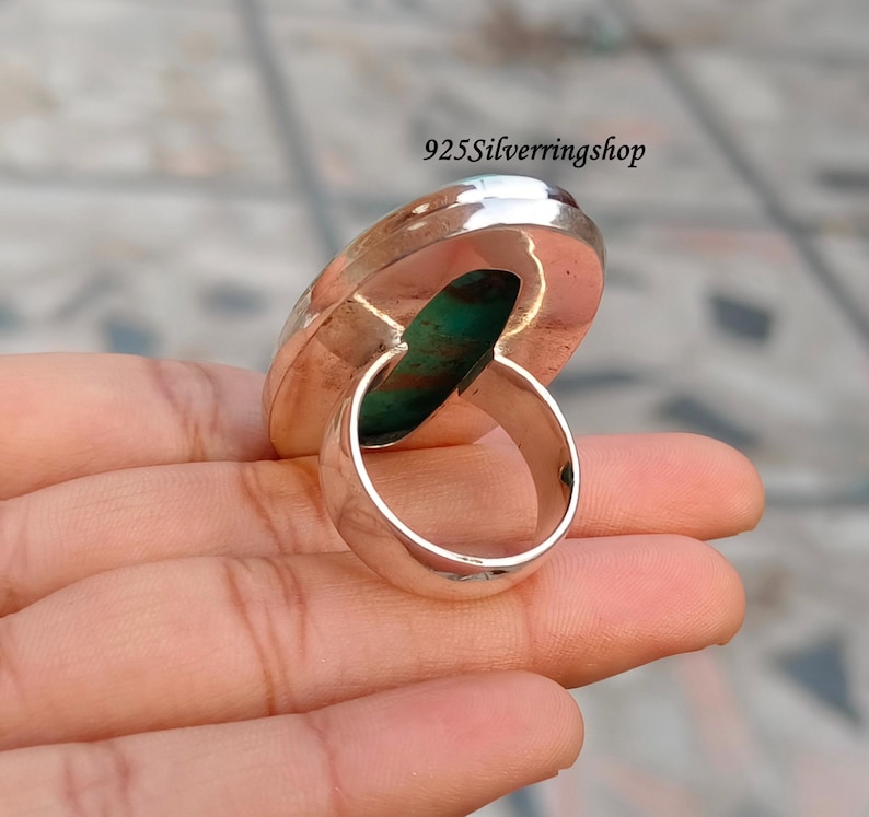 May include: A silver ring with a large, oval turquoise stone. The ring has a wide band and a polished finish. The stone is a vibrant turquoise color with brown and green marbling. The text "925Silverringshop" is visible.