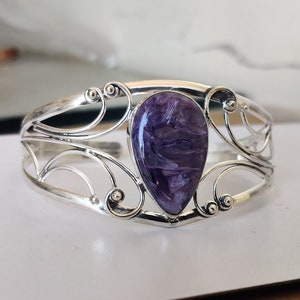 Pode incluir: Um bracelete de prata com uma gema roxa e branca no centro. O bracelete tem um design delicado e ornamentado.