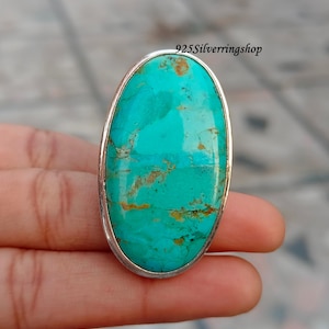May include: A large, oval turquoise gemstone ring with a silver band. The turquoise stone is a vibrant blue-green color with brown veining. The ring is held in a hand, and the text "925Silverringshop" is visible.