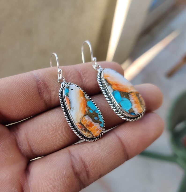 May include: A pair of silver dangle earrings with oval-shaped turquoise stones. The stones are a mix of white, orange, and blue.