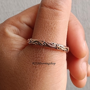 May include: A close-up of a gold-colored ring with a floral design. The ring is on a finger. The ring has a repeating pattern of leaves and vines. The text "925Silverringshop" is visible.