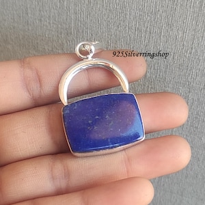 May include: A silver pendant with a dark blue lapis lazuli stone. The pendant is shaped like a small rectangular box with a rounded top.