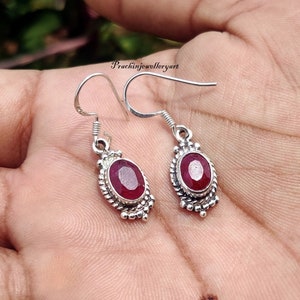 Pode incluir: Um par de brincos de prata com pedras ovaladas vermelhas. Os brincos têm um design delicado com pequenas contas em torno das pedras.