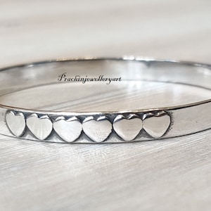 May include: A silver bangle bracelet with a row of heart-shaped indentations.