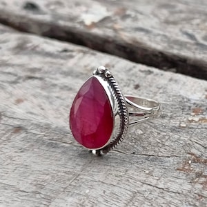 Peut inclure: Une bague en argent avec une pierre précieuse rouge en forme de larme sertie dans un entourage en argent détaillé.
