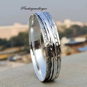 May include: A silver spinning ring with a textured design. The ring has three bands that spin independently.