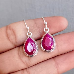 May include: A pair of silver dangle earrings with teardrop-shaped ruby gemstones.