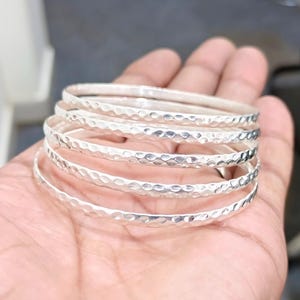 May include: A set of five silver bangles with a hammered texture. The bangles are stacked on top of each other.