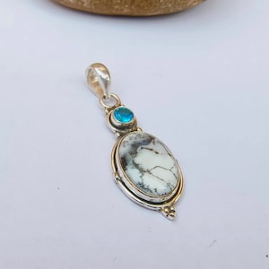 May include: A silver pendant with a white and gray oval stone and a blue gemstone. The pendant has a silver bail for attaching to a chain.