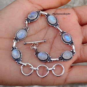 May include: A silver bracelet with a toggle clasp and oval-shaped moonstone gemstones. The bracelet has a delicate, intricate design.