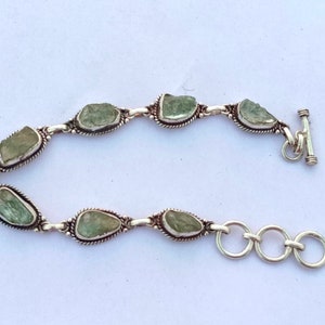 May include: A silver bracelet with a chain link design and green gemstone accents. The bracelet has a toggle clasp.