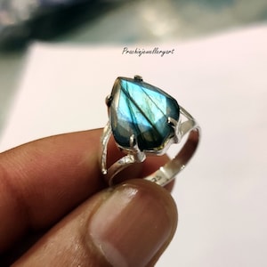 May include: A silver ring with a large, faceted, iridescent blue labradorite gemstone. The ring has a delicate, openwork design.