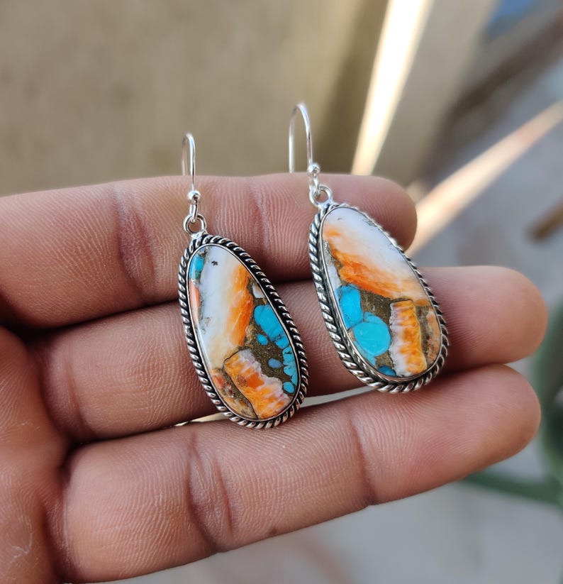May include: A pair of silver dangle earrings with turquoise and orange stone accents. The stones are oval shaped and have a unique, marbled pattern.