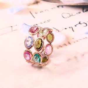 May include: A rose gold ring featuring a double row of oval-shaped gemstones in a variety of colours, including pink, blue, green, and yellow.