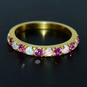 Op de afbeelding: Een gouden bandring met afwisselend roze en witte edelstenen. De ring heeft een doorlopende rij ronde edelstenen, wat een sprankelend en elegant ontwerp creëert. De edelstenen zijn gezet in een gouden band.