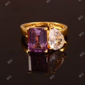 May include: A gold ring with a purple emerald-cut gemstone and a clear pear-shaped gemstone.