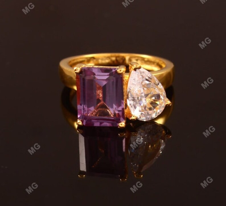 May include: A gold ring with a purple emerald-cut gemstone and a clear pear-shaped gemstone.