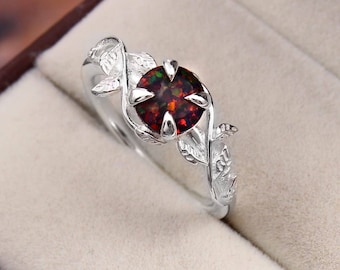 May include: A silver ring featuring a round, dark-colored stone with red and green iridescent flecks. The band is designed with a textured leaf motif that wraps around the central stone, which is held in place by four polished silver prongs.