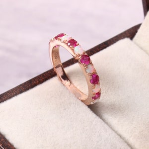 Op de afbeelding: Een roségouden bandring met afwisselende witte opaal- en roze robijnstenen.