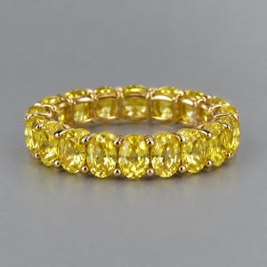 Peut inclure: Une bague alliance composée d'une rangée continue de pierres précieuses jaunes taille ovale, serties dans une monture en métal doré poli. La bague présente un agencement uniforme de pierres jaunes facettées et éclatantes sur tout le tour.