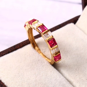 May include: A gold band ring with alternating red ruby and clear baguette-shaped diamonds.