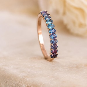 Peut inclure: Une bague en or rose ornée d'une rangée de dix pierres précieuses de taille ovale, passant du violet profond et magenta à la base au bleu et turquoise vifs au sommet, serties dans une monture à griffes partagées sur la moitié de l'anneau.