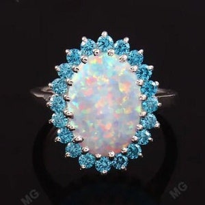 May include: A silver ring featuring a large oval opal set within a halo of smaller blue gemstones.