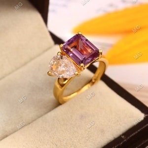 May include: A gold ring with a large, rectangular, purple amethyst gemstone and a smaller, pear-shaped, clear diamond gemstone.