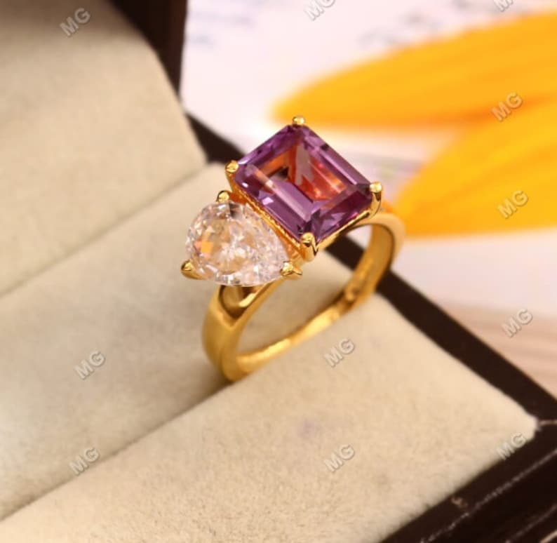 May include: A gold ring with a large, rectangular, purple amethyst gemstone and a smaller, pear-shaped, clear diamond gemstone.